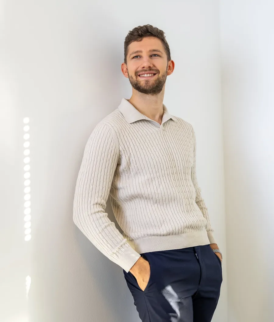 Daniel Wegener lächelnd im hellen Pullover, an eine Wand gelehnt